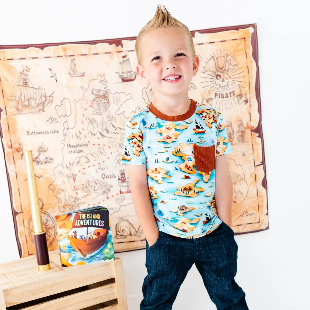 Child wearing a pirate-themed shirt with a map and treasure chest in the background