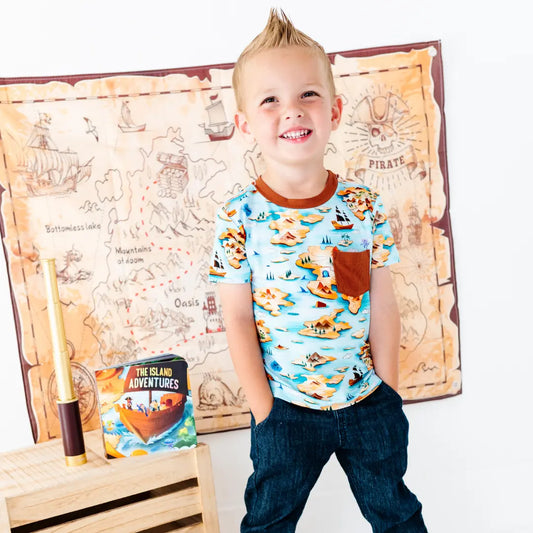Child wearing a pirate-themed shirt with a map and treasure chest in the background