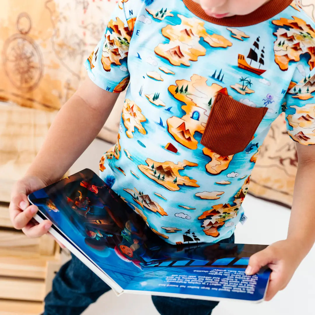 Child wearing a pirate-themed shirt holding a book with a similar design.