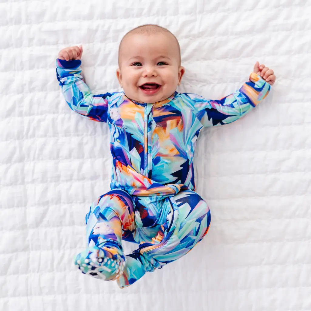 Baby wearing a colorful onesie on a white textured surface