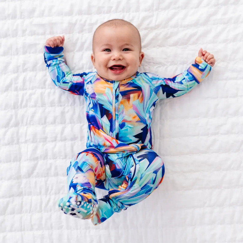 Baby wearing a colorful onesie on a white textured surface
