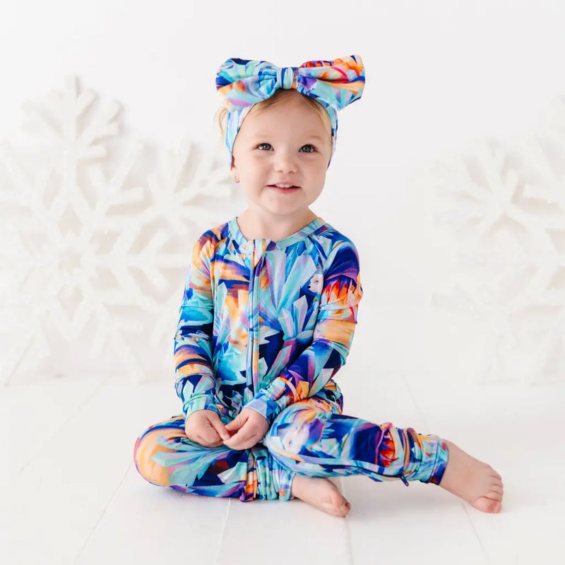 Baby wearing a colorful onesie and headband on a white background