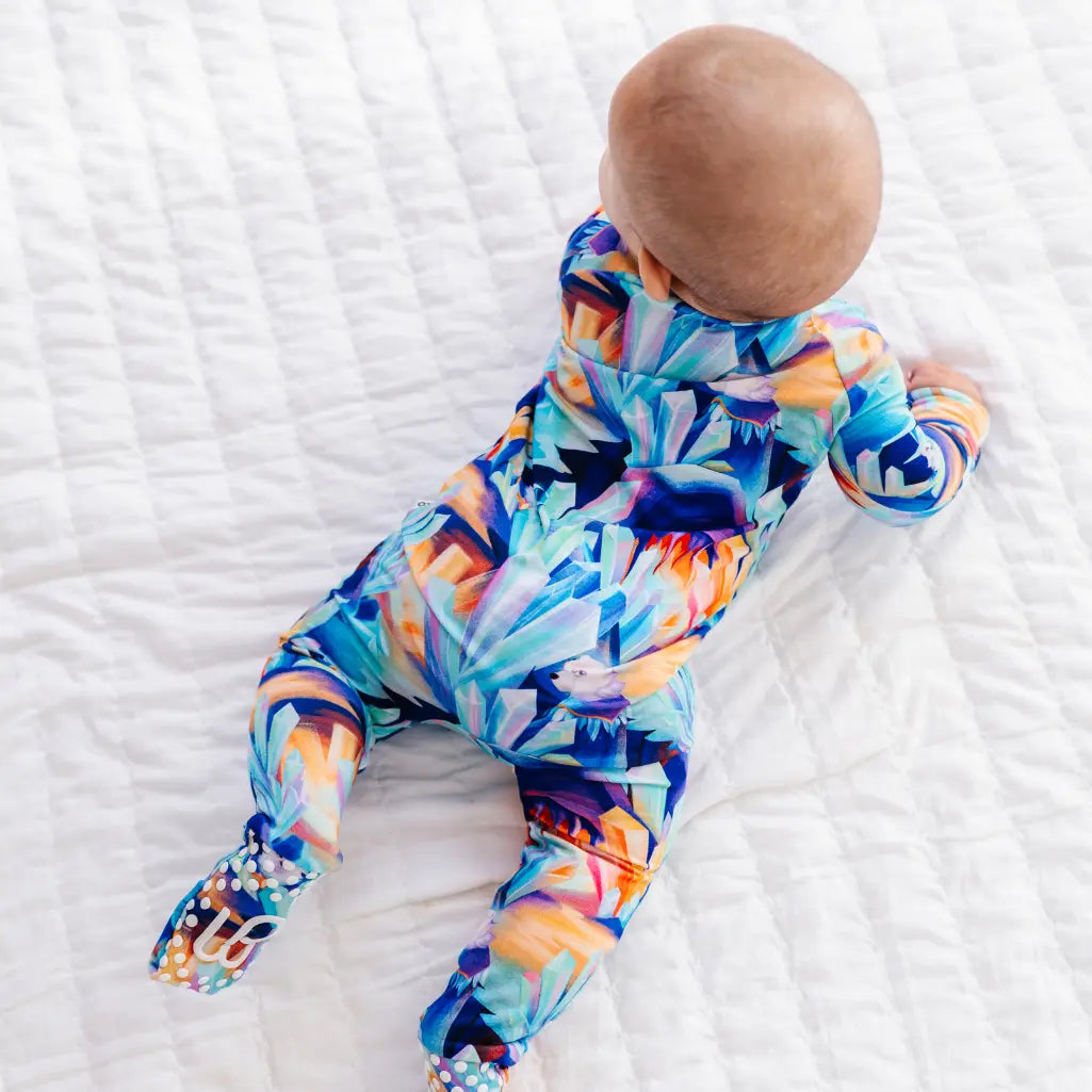 Baby wearing a colorful onesie on a white textured surface