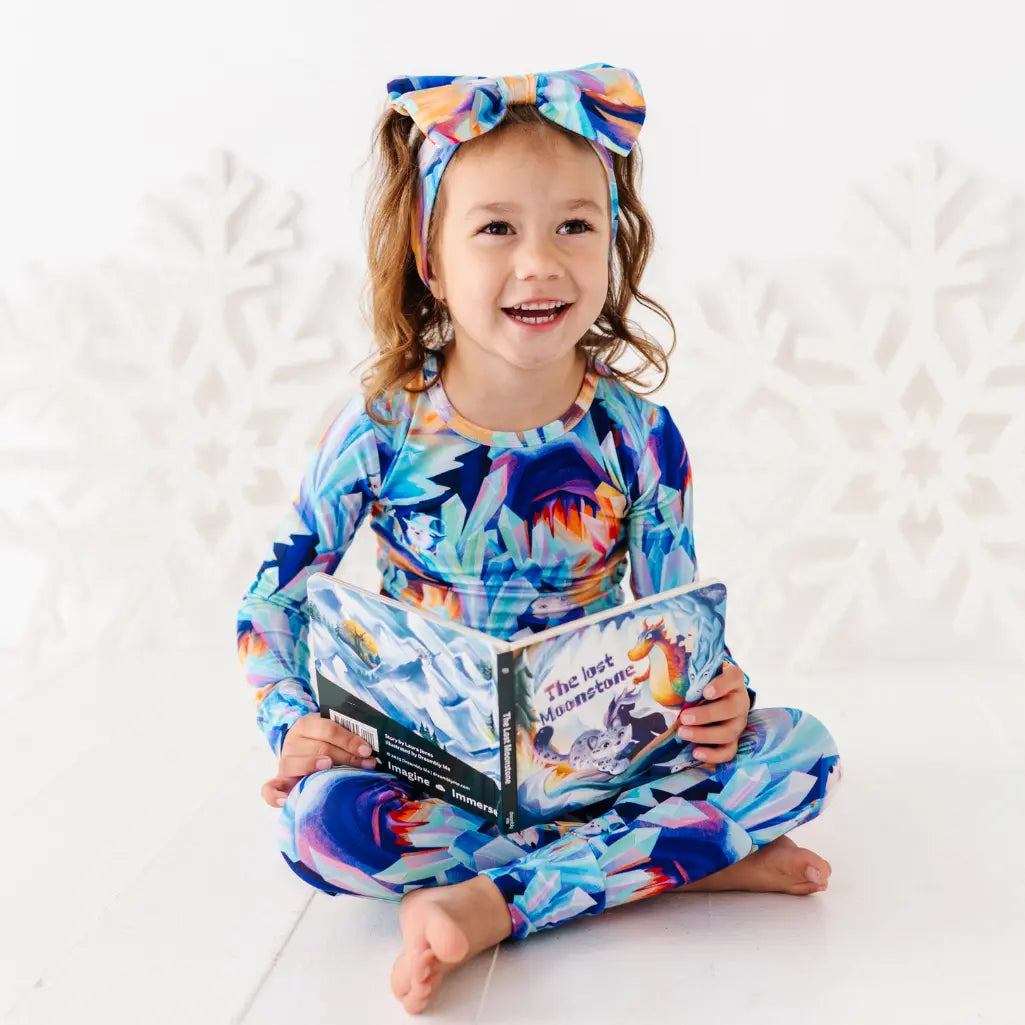 Child wearing a colorful outfit with a floral pattern, holding a book on a white background