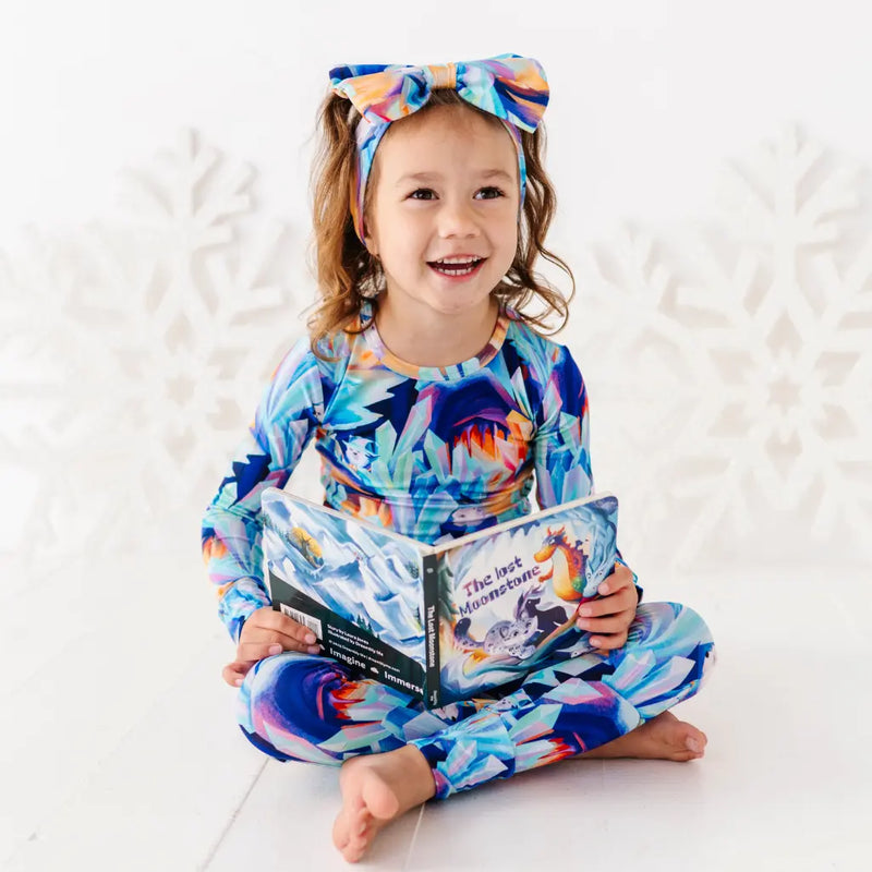 Child wearing a colorful outfit with a floral pattern, holding a book on a white background