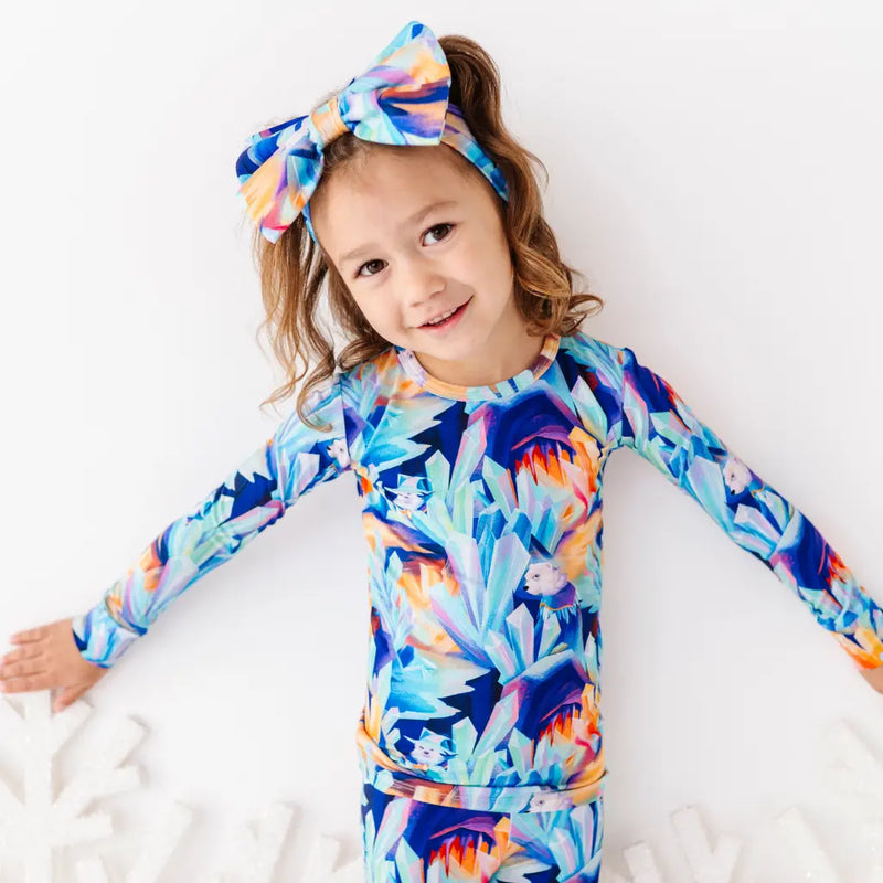 Child wearing a colorful floral long-sleeve shirt and headband on a white background