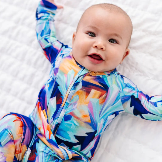 Baby wearing a colorful outfit with abstract patterns on a white blanket