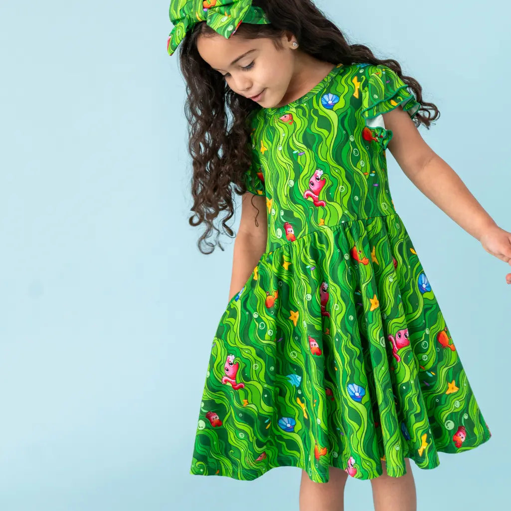 Young girl wearing a green dress with colorful patterns against a light blue background