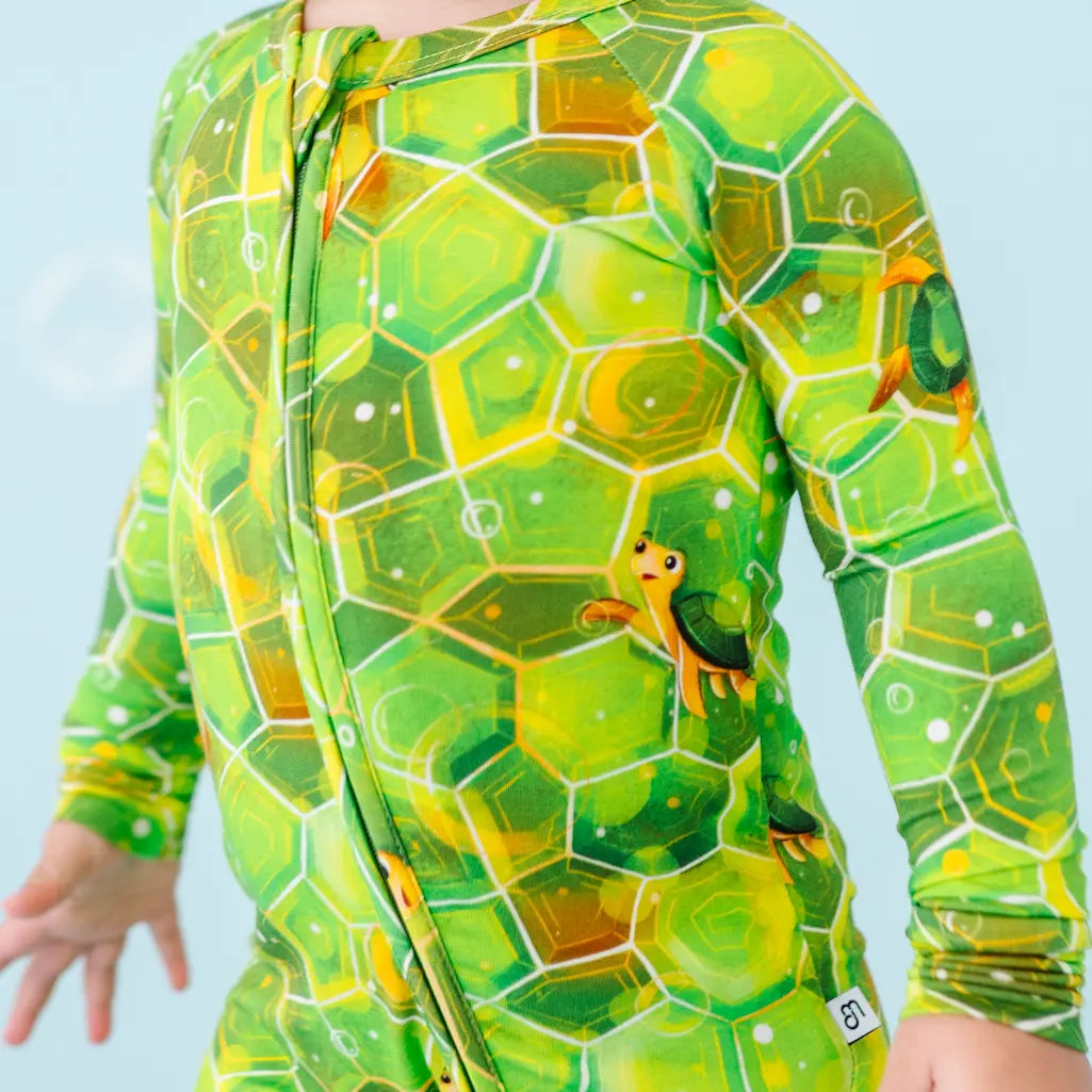 Child wearing a green and yellow patterned onesie against a light blue background