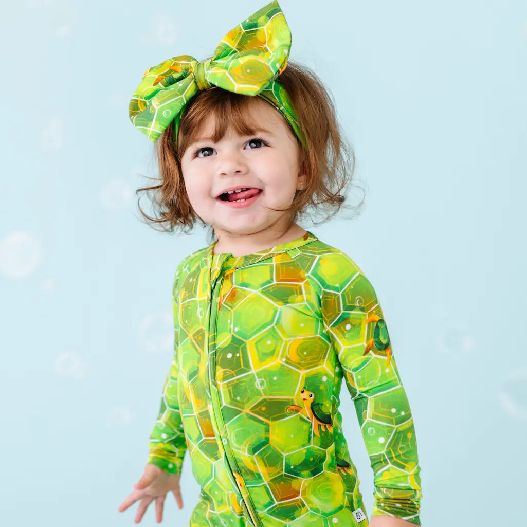 Child wearing a green geometric patterned outfit and headband against a light blue background.