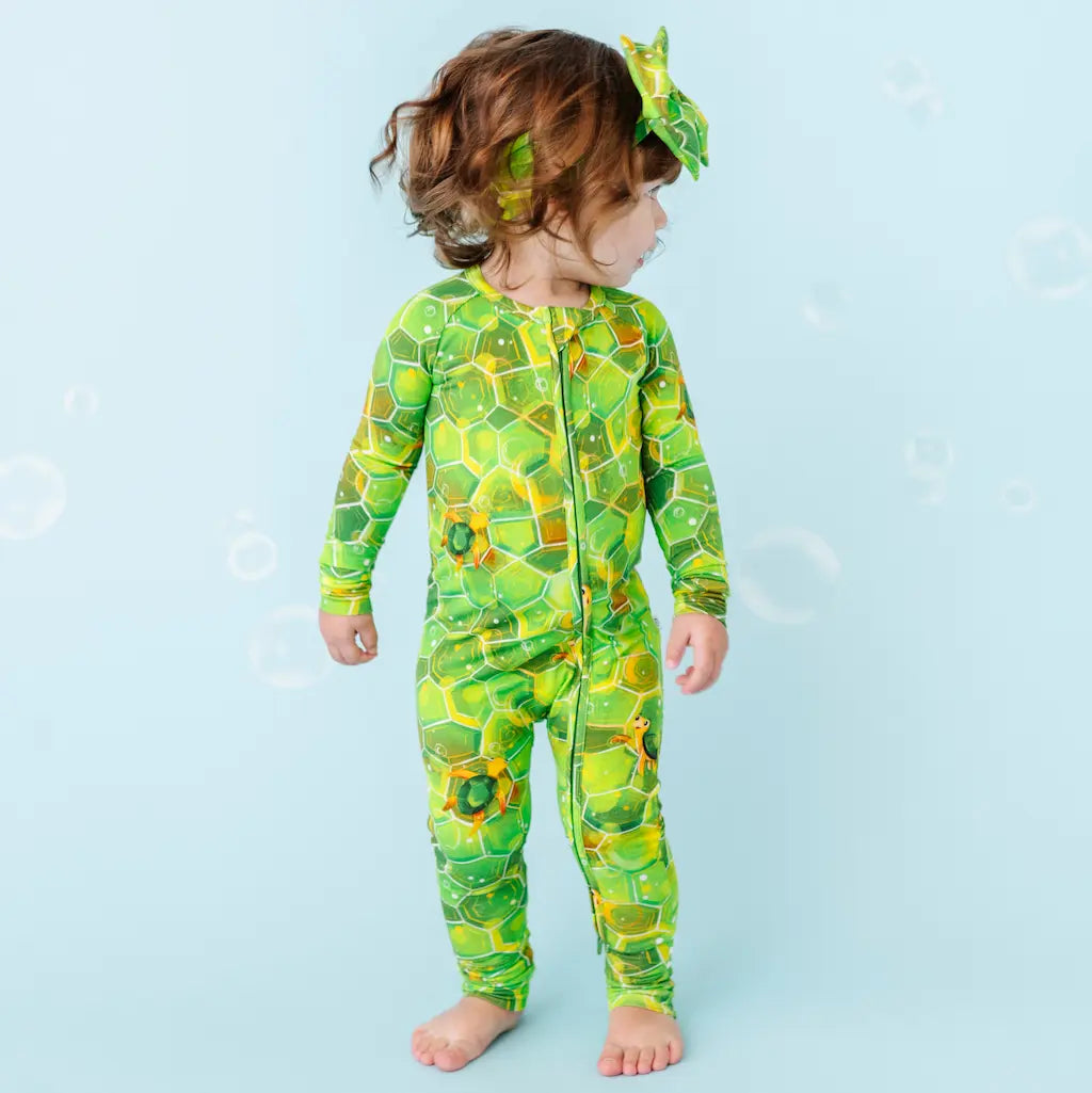 Child wearing a green dinosaur-themed onesie on a light blue background.