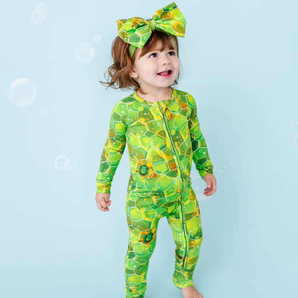 Child wearing a green geometric patterned outfit with a matching headband on a light blue background.