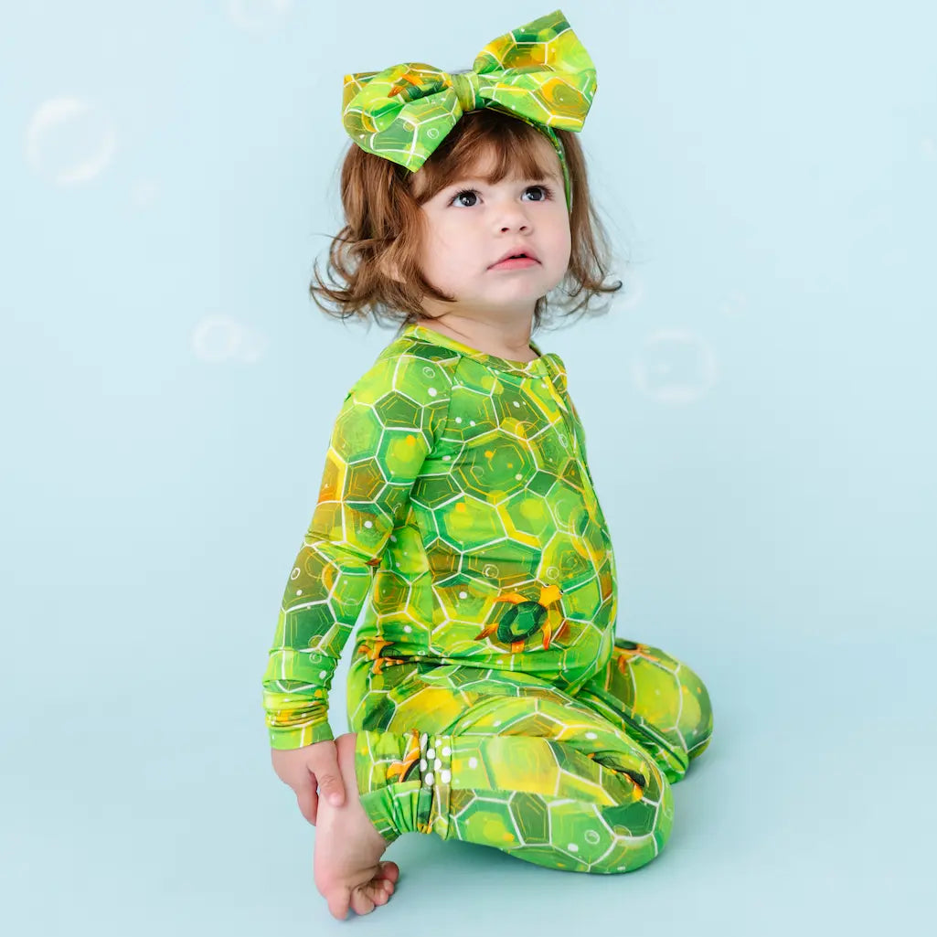 Child wearing a green honeycomb pattern outfit with a matching headband on a light blue background.