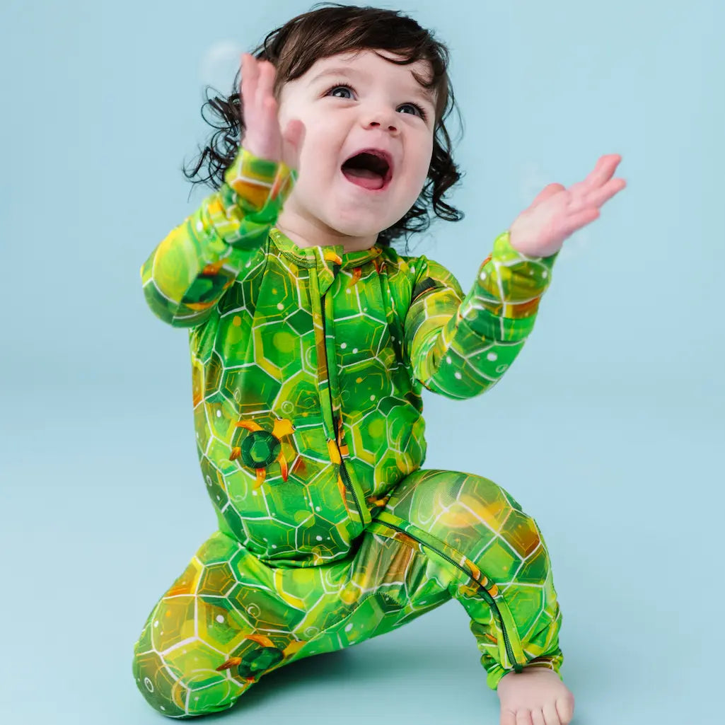 Child wearing a green turtle-themed onesie on a blue background.