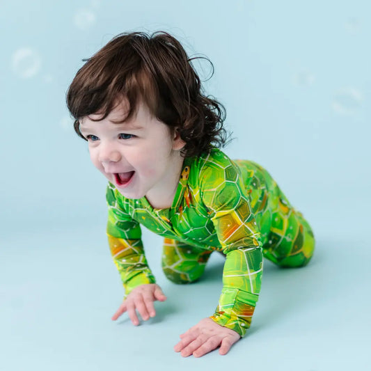 Child wearing a green and yellow patterned onesie on a blue background
