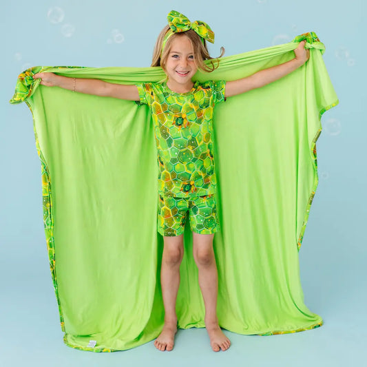 Child in green floral outfit with matching cape on a plain background