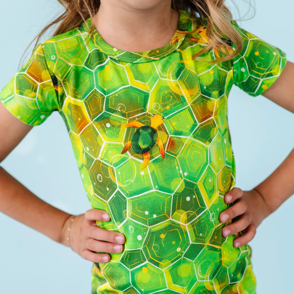 Child wearing a green and yellow geometric patterned shirt against a light blue background.