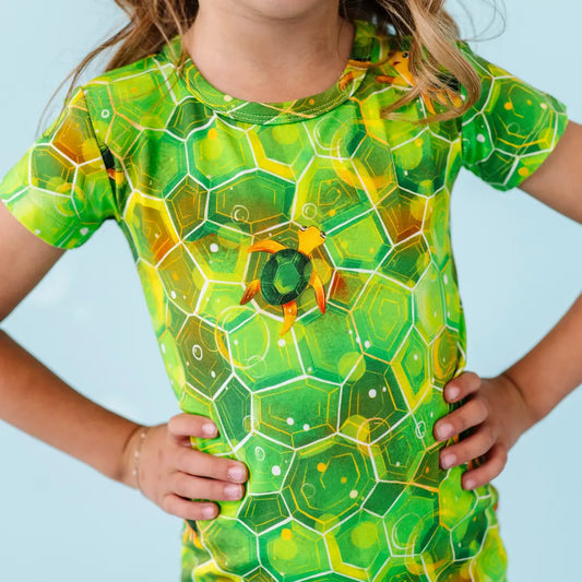 Child wearing a green and yellow geometric patterned shirt against a light blue background.