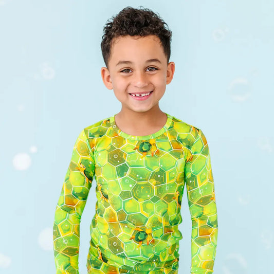 A child wearing a long-sleeved top and pants with a geometric green sea turtle pattern.