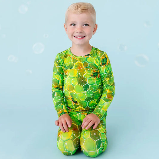 A child wearing a long sleeve top and matching pants with a geometric green sea turtle pattern.