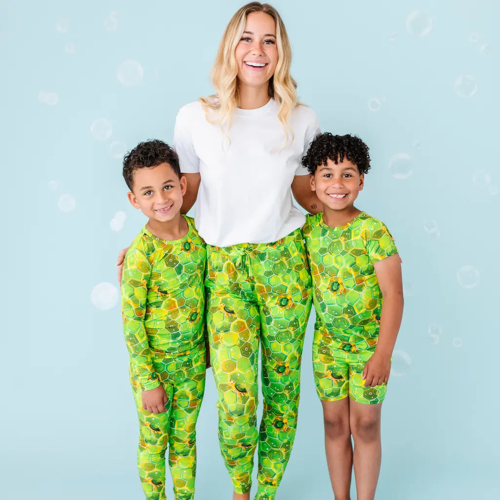 Woman and two children wearing matching green patterned outfits on a light blue background