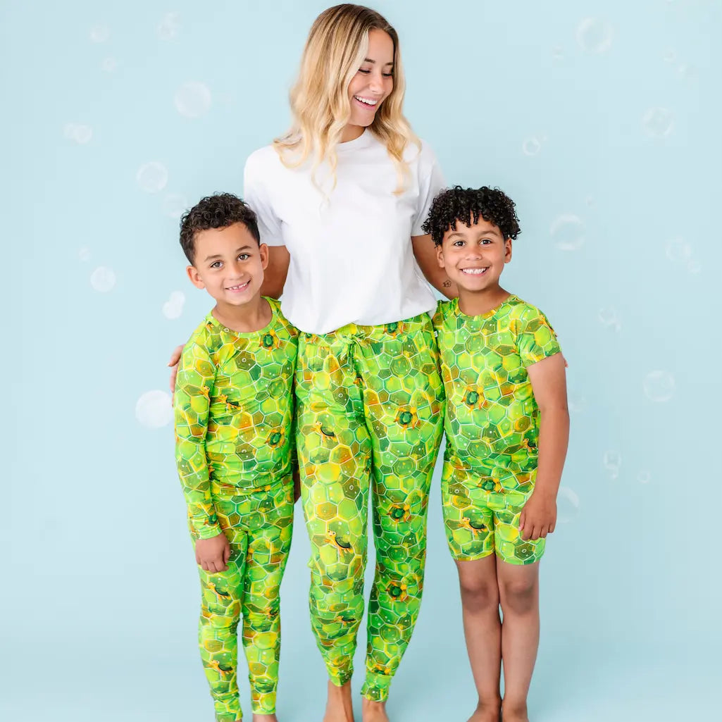 Woman and two children in matching green floral outfits on a light blue background.