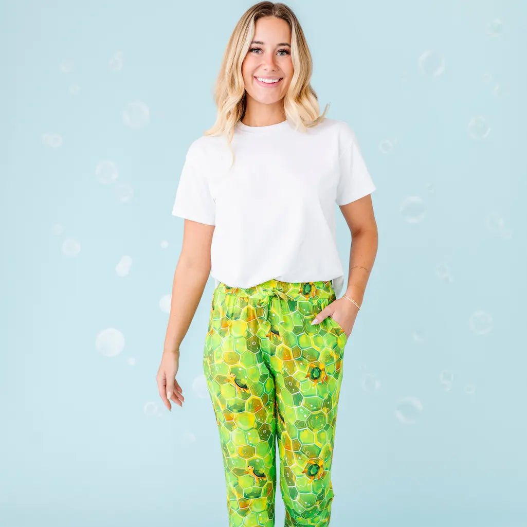 Woman wearing a white t-shirt and green patterned pants on a light blue background