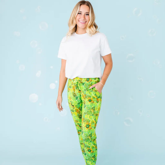 A woman standing and smiling, wearing white shirt and green pajama pants with a geometric turtle pattern.