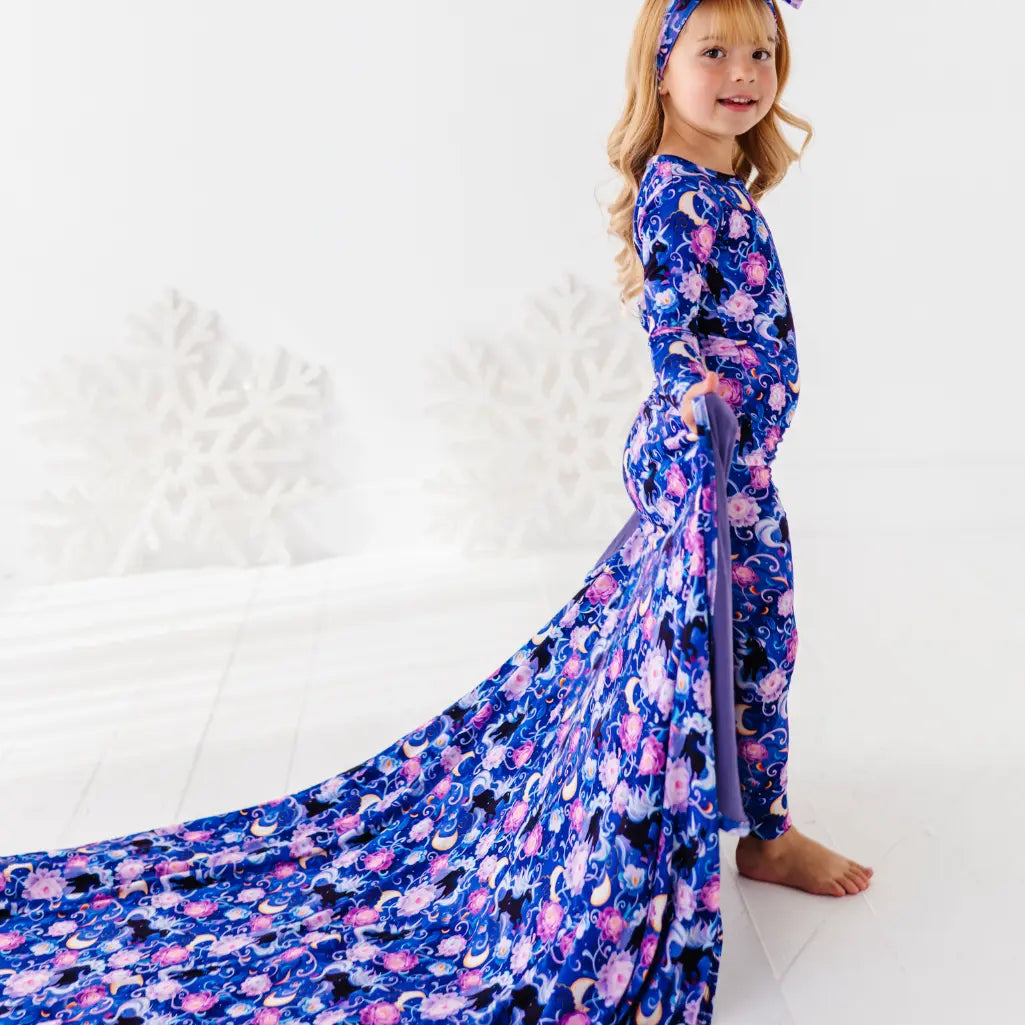 Young girl wearing a long, colorful floral dress with a matching headband on a white background