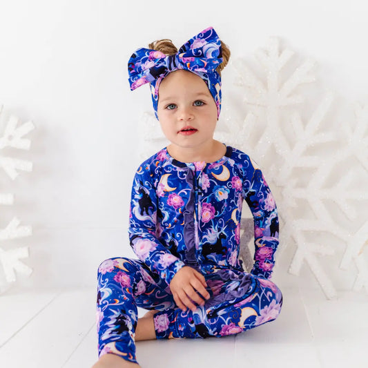 Child wearing a colorful onesie with a floral and moon design on a white background