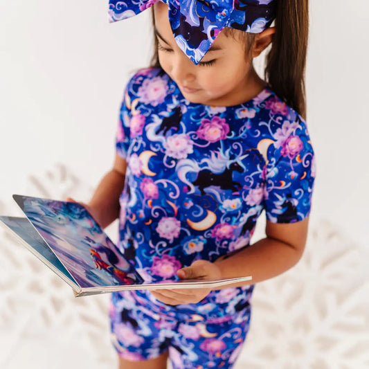 Child wearing a colorful outfit with a pattern of cats, flowers, and moons, holding a book.