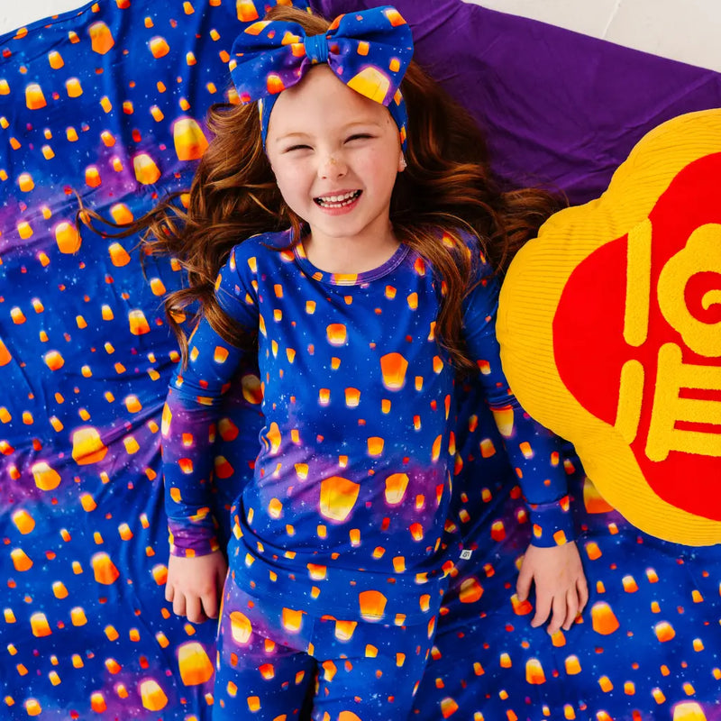 Child wearing a blue outfit with orange polka dots, lying on a colorful blanket with a large yellow and red emblem.