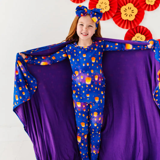 Child wearing a colorful outfit with a purple cape against a white background