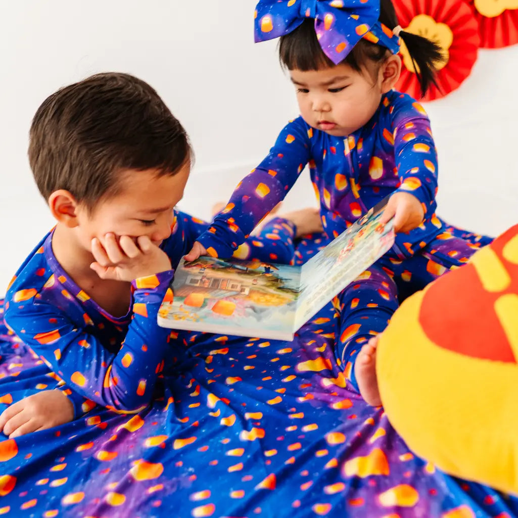Two children in matching blue outfits with orange polka dots reading a book.