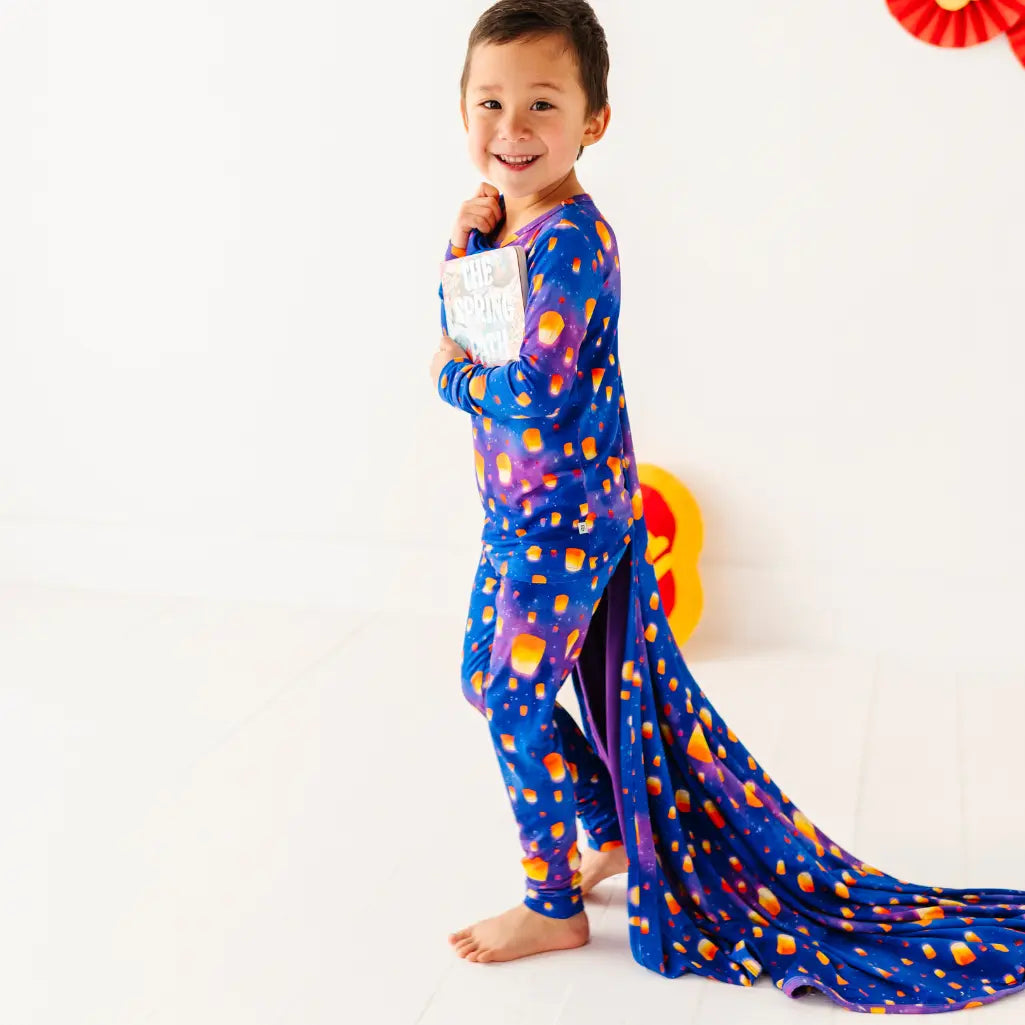 Child wearing a colorful onesie with a long tail, holding a book, on a white background.