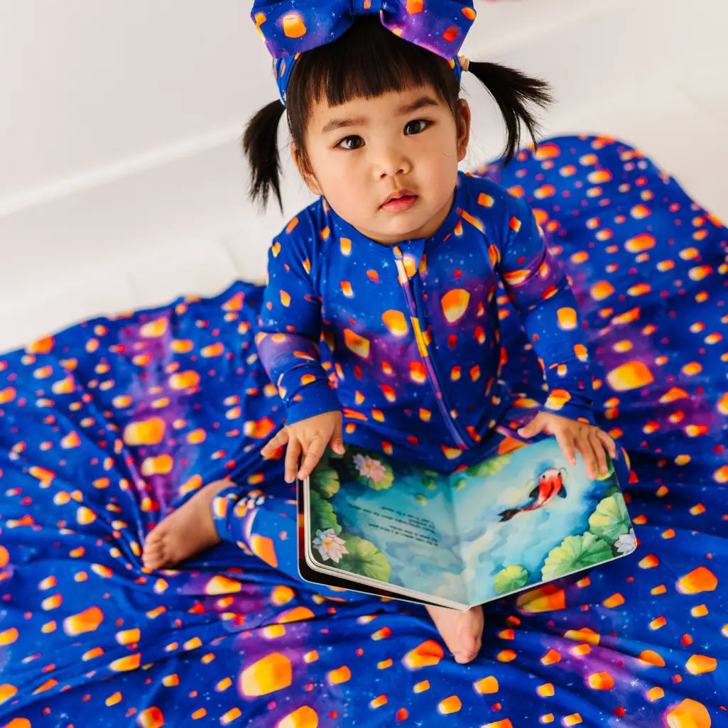 Child in a colorful outfit holding a book on a matching blanket