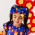Child wearing a colorful shirt and headband with candy corn design against a floral background