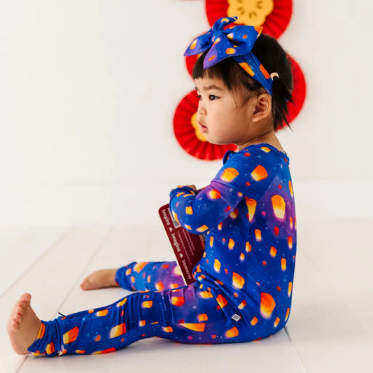 Child wearing a colorful outfit with a blue bow, sitting on a white floor.