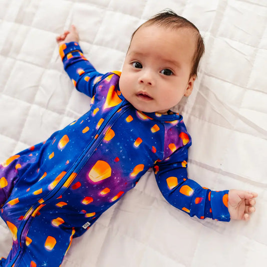 Baby wearing a colorful onesie with orange polka dots on a white textured surface