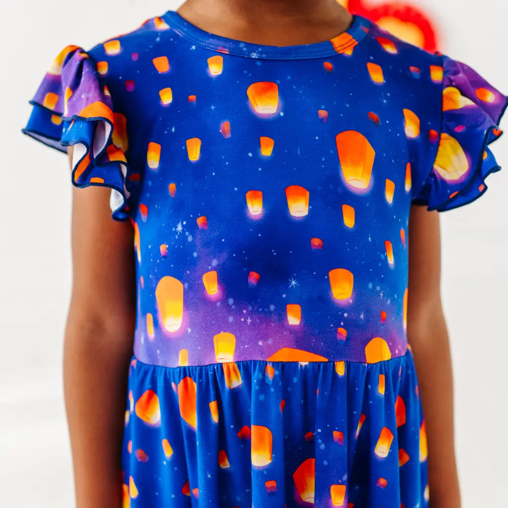 Child wearing a blue dress with colorful lantern pattern on a white background