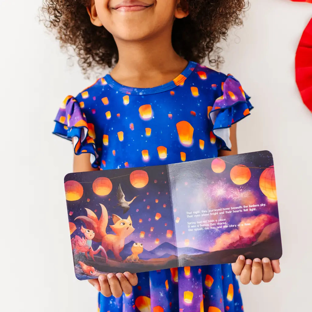 Child holding a colorful book with a fox and moon illustration, wearing a matching dress.