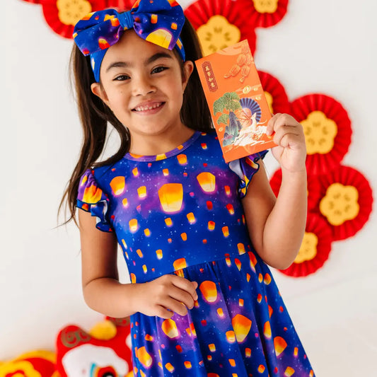 Young girl in a colorful dress holding a red envelope against a decorative background