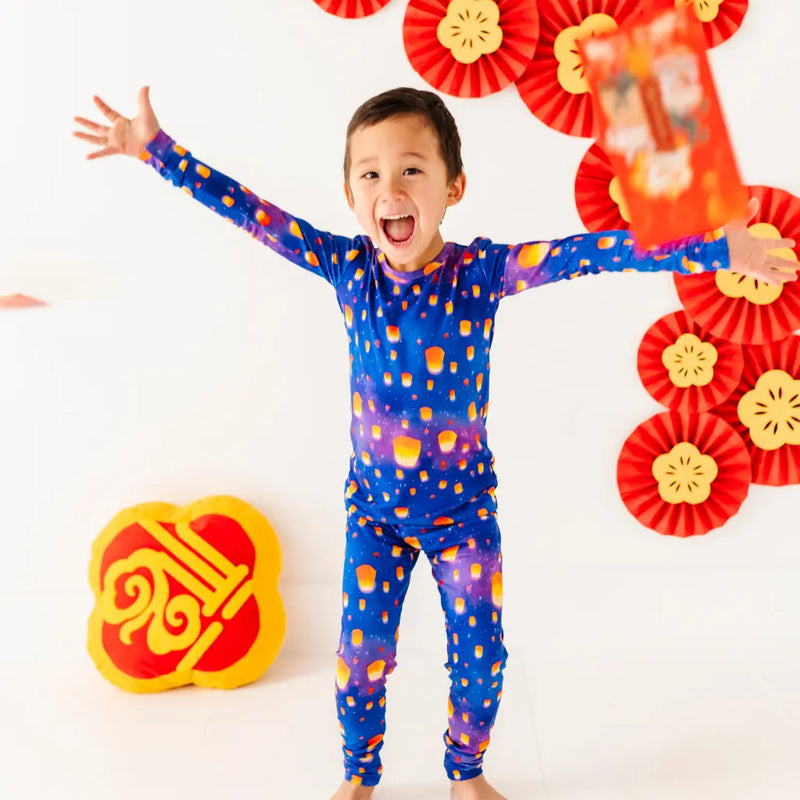 Child wearing a colorful outfit with arms outstretched, surrounded by red and gold decorations on a white background