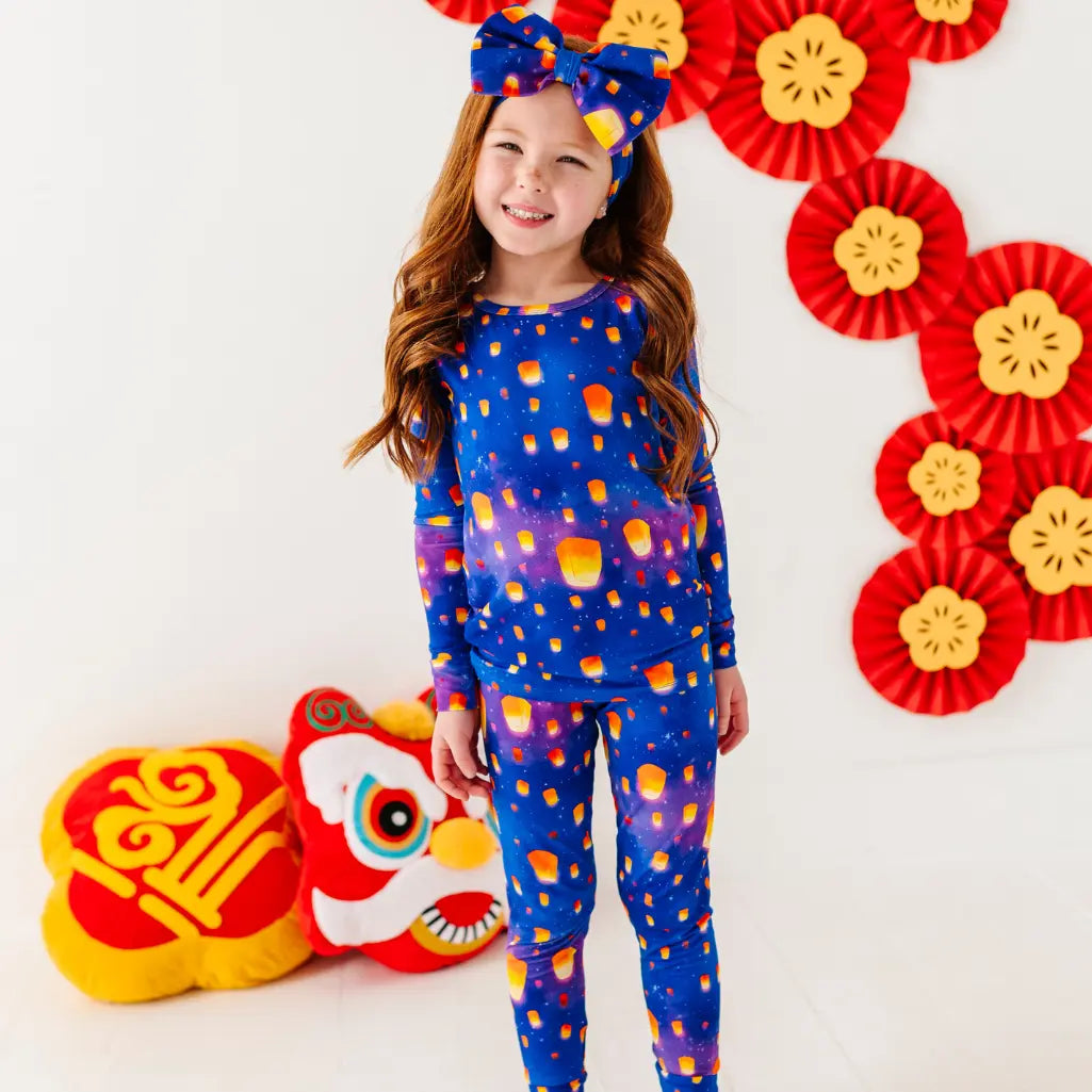 Child wearing a blue outfit with orange patterns, standing in front of red and yellow decorations.