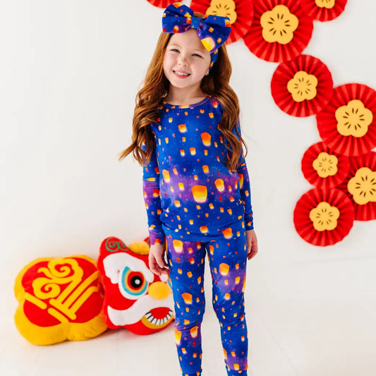 Child wearing a blue outfit with orange patterns, standing in front of red and yellow decorations.