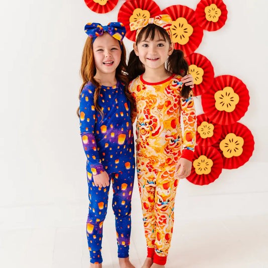 Two children wearing colorful pajamas with decorative headbands and a floral backdrop.