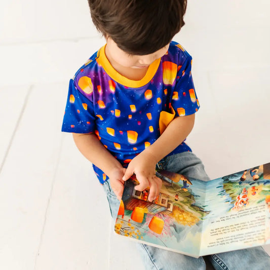 Child wearing a colorful shirt with candy corn pattern, reading a book.