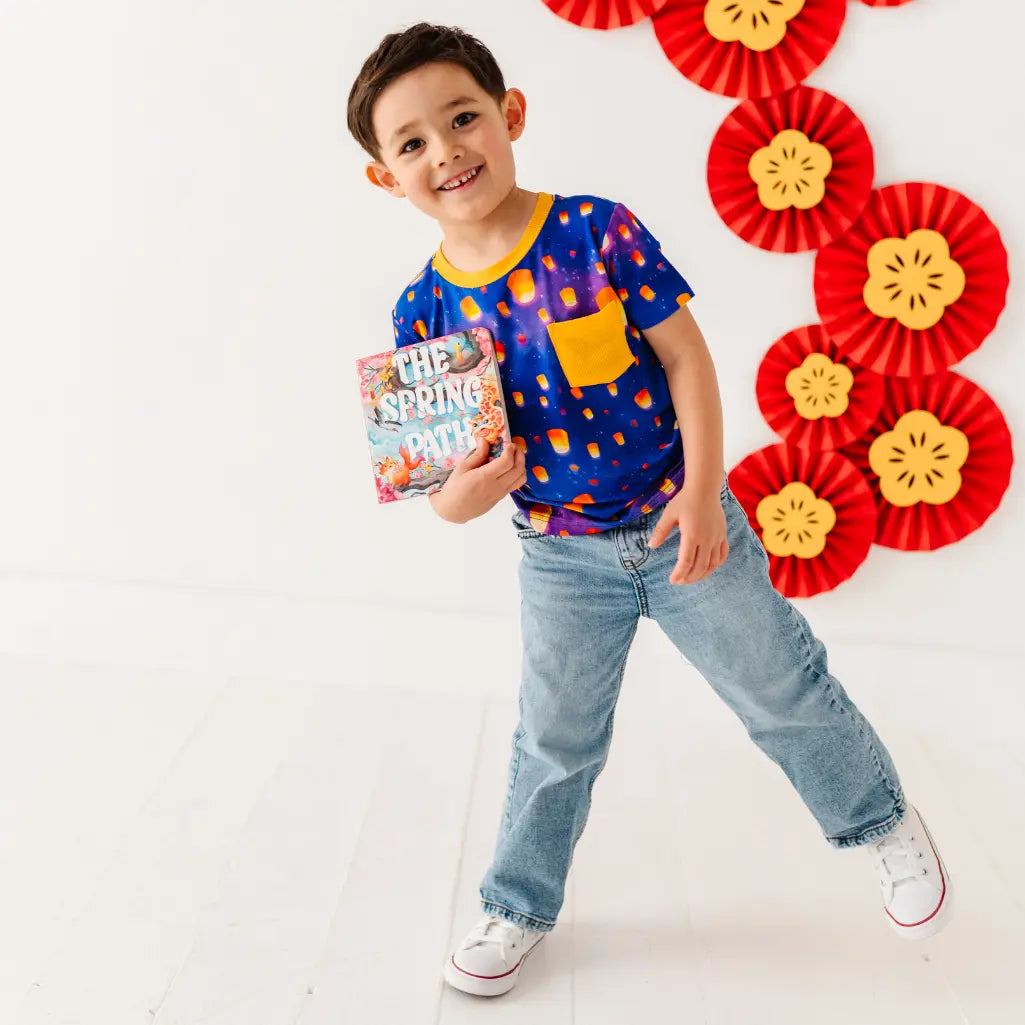 Child wearing a colorful shirt and jeans, holding a book, with decorative red and yellow elements in the background.