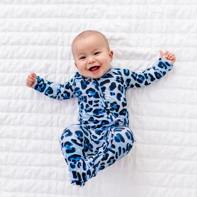 Baby wearing a blue leopard print onesie on a white blanket