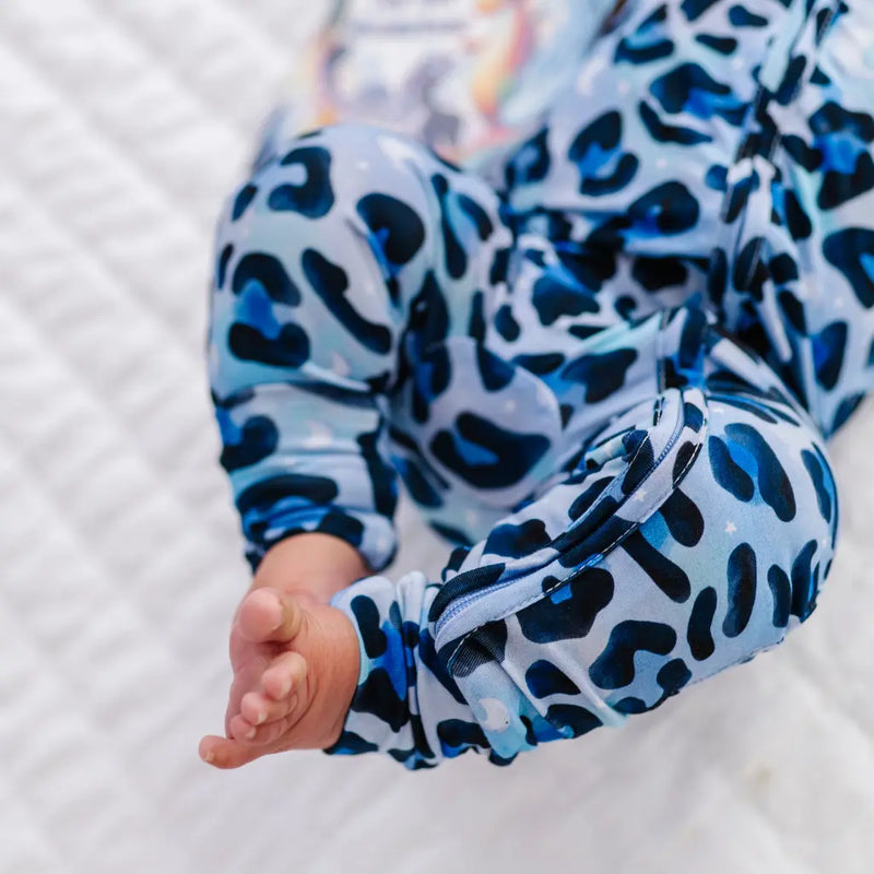 Baby's legs wearing blue and black leopard print pants on a white blanket.